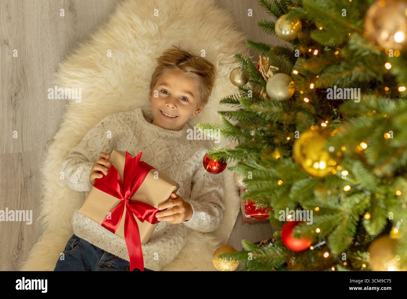 Garçon préscolaire mignon, assis devant la cheminée, tenant un cadeau de noël et lisant un livre, joie et bonheur à la maison Banque D'Images