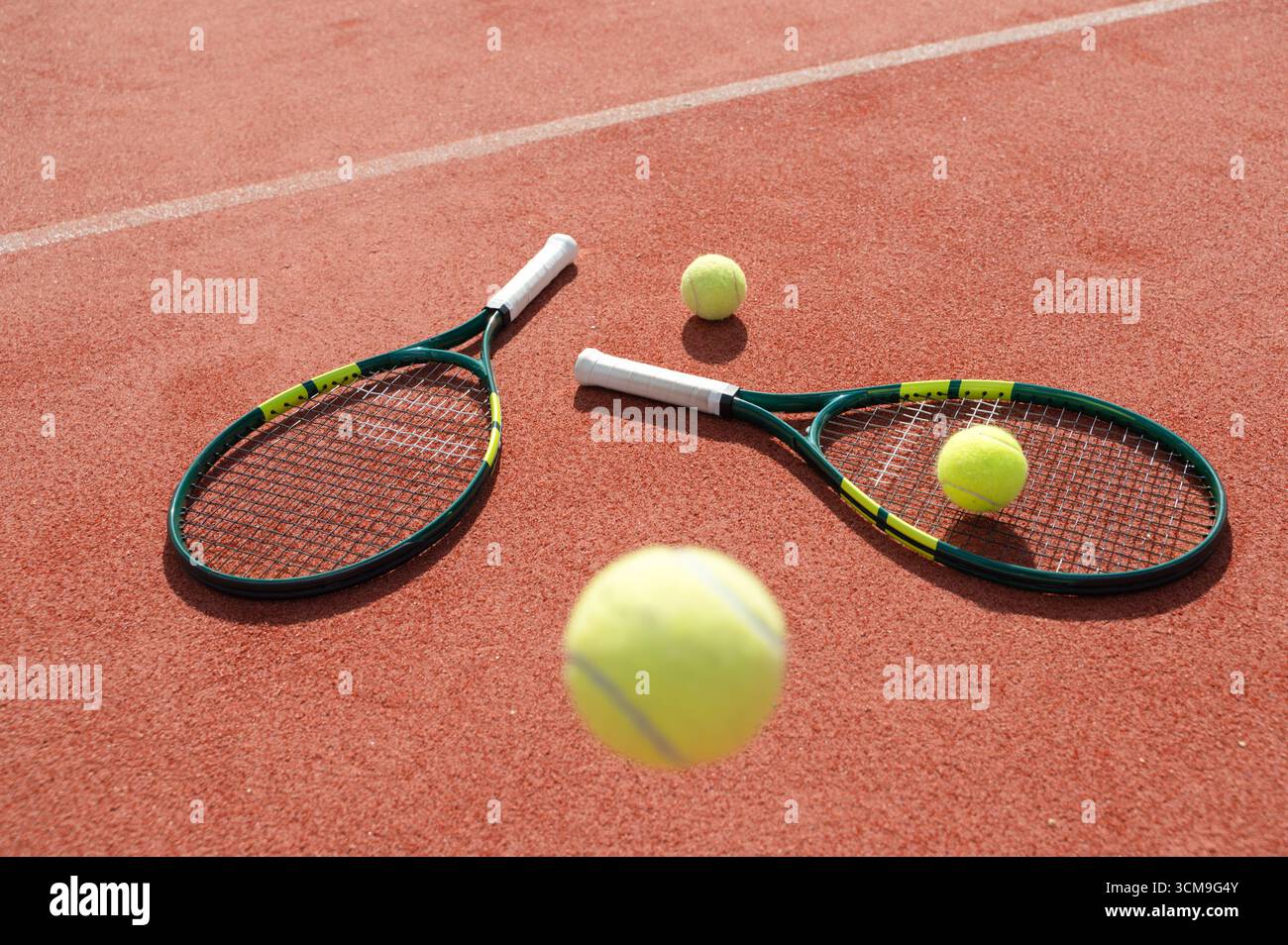 Deux raquettes de tennis, accompagnées de balles, sont présentées sur un terrain de terre battue rouge vif et éclatant Banque D'Images