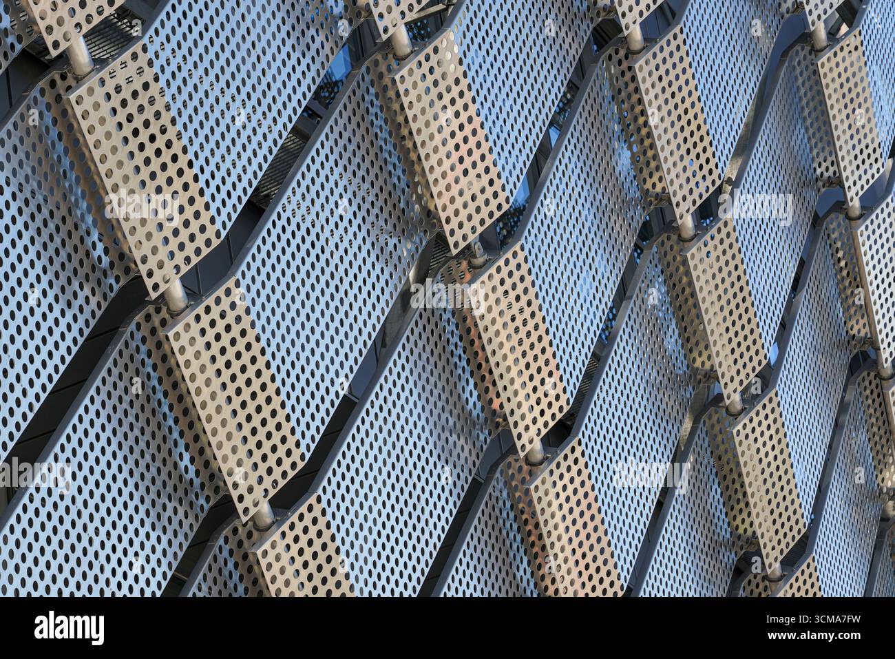 Suède, Stockholm, façade de Tele2 Arena, conçu par White Arkitekter. Des rangées de panneaux métalliques perforés créent un motif dynamique. Chaque trou méticuleusement aligné pour former un treillis complexe. Interaction de la lumière et de l'ombre. L'éclat métallique reflète le ciel et les environs. Banque D'Images