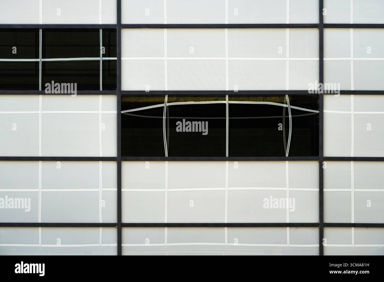 Distorsions inattendues : échos courbes. Une façade à Stockholm, en Suède, montre des lignes de grille noires strictes contrastant avec des reflets incurvés blancs sur les vitres, où les distorsions environnantes brisent la géométrie et ajoutent une complexité dynamique au design moderne. Banque D'Images