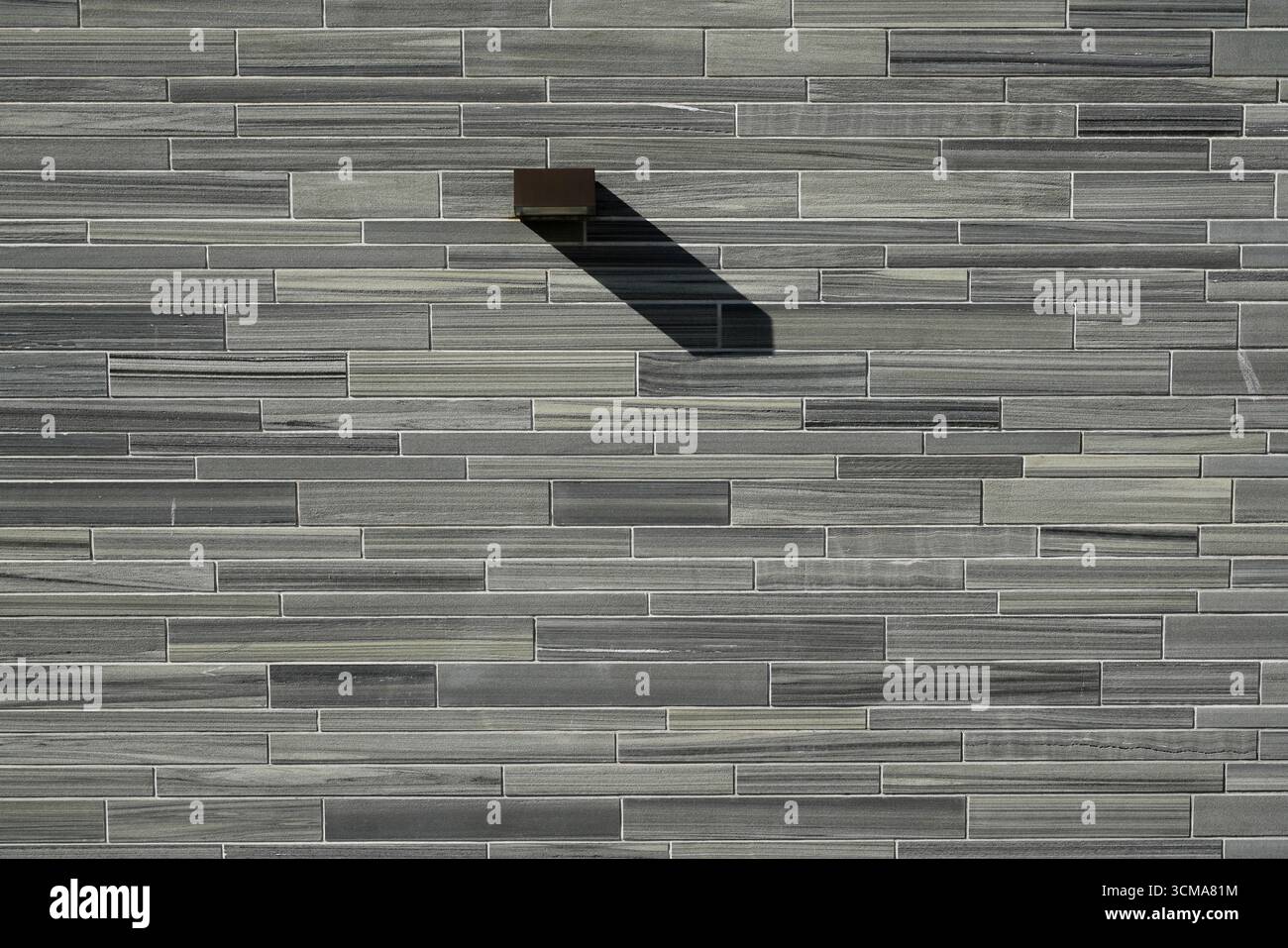 Interaction de lumière et d'ombre : rythmes architecturaux. Le Musée National d'Oslo, Norvège conçu avec une façade carrelée révèle un alignement précis d'éléments en pierre, où une lampe murale projette une ombre géométrique qui rehausse le rythme de la surface. Banque D'Images