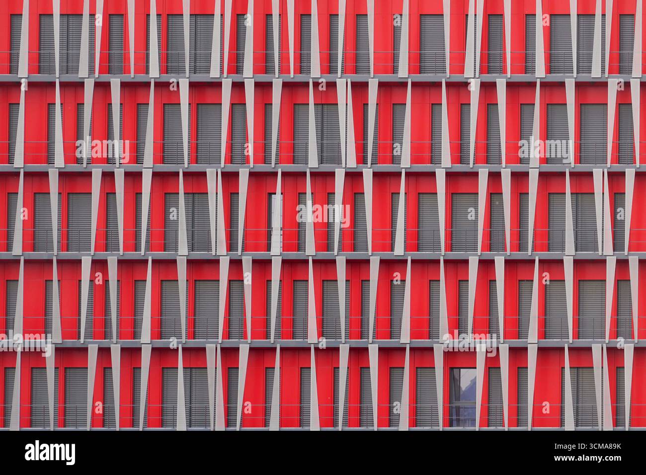 Échiquier urbain : motif rythmique. Une façade à Grenoble, conçue par SOHO Architects Lyon, montre des panneaux rouges audacieux avec des volets gris disposés en rythme damier. Les obturateurs alternés ajoutent de l'individualité dans l'uniformité géométrique. Banque D'Images