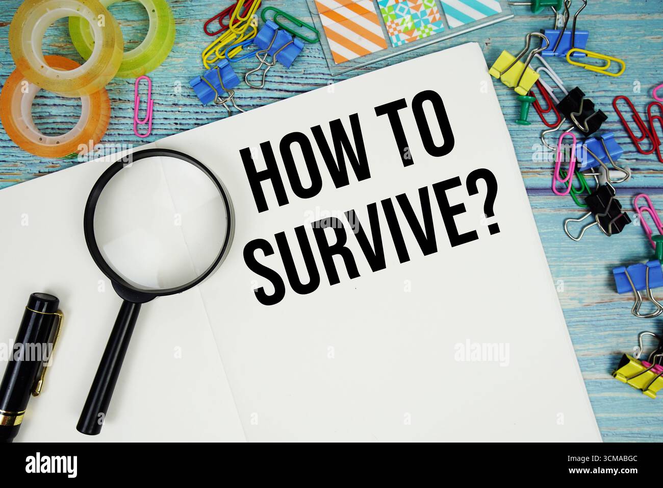 Comment survivre ? texte écrit sur bloc-notes avec loupe plate sur fond en bois Banque D'Images