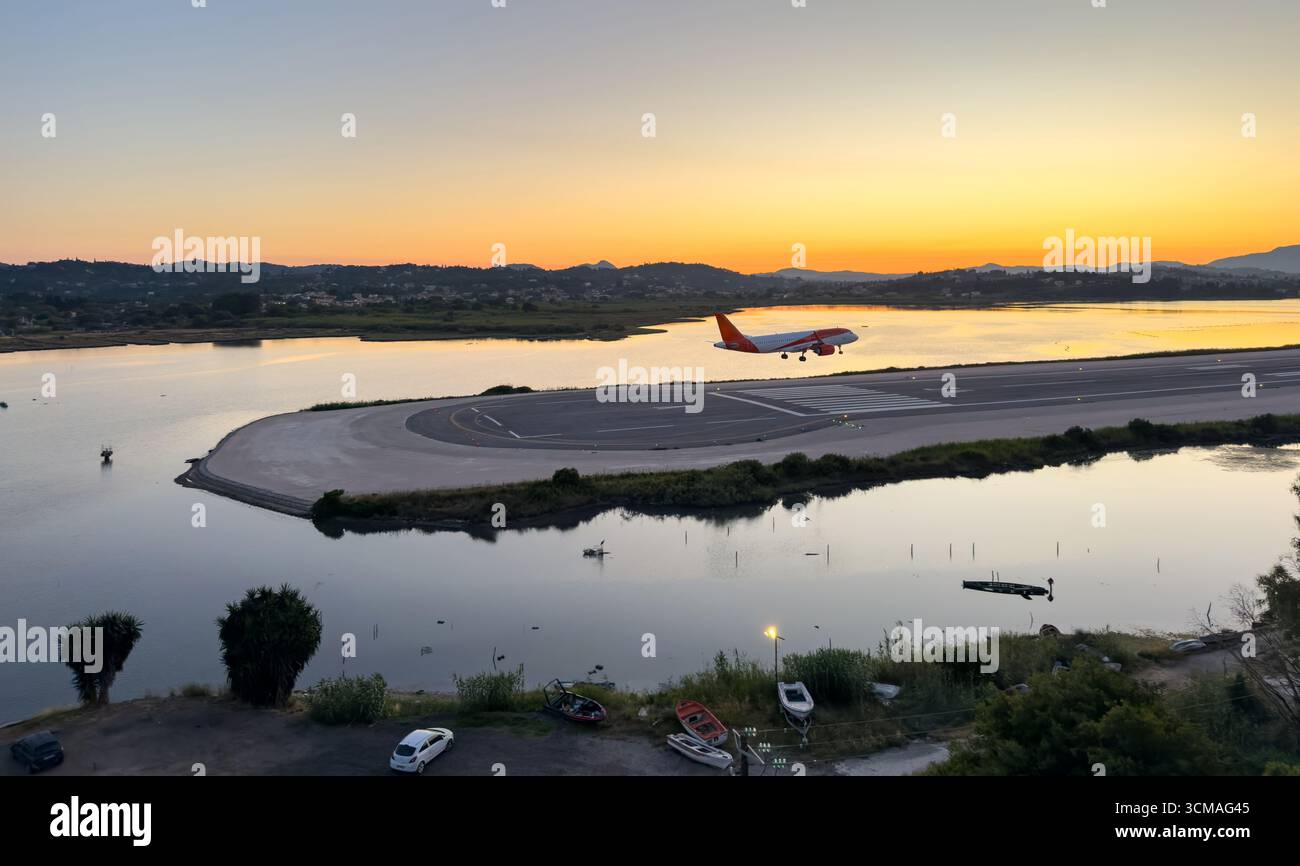 Un avion commercial descend vers la piste de l'aéroport de Corfou au coucher du soleil, en Grèce. Eau calme, collines lointaines et lumière chaude du soir Banque D'Images