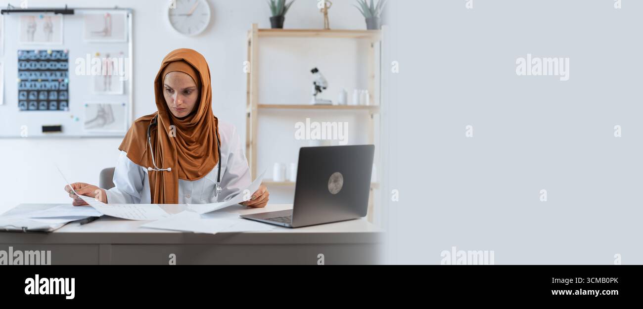 Jeune femme musulmane médecin travaillant avec un ordinateur portable et lisant des documents faisant de la paperasse. Cabinet hospitalier. bannière. copier l'espace Banque D'Images