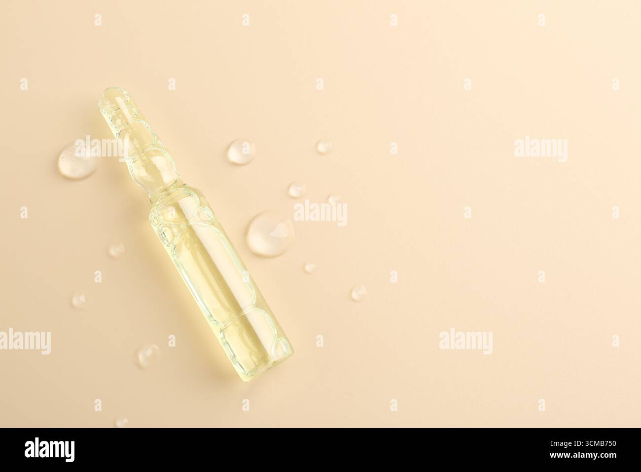 Ampoule en verre avec produit cosmétique et gouttes d'eau sur fond beige, vue de dessus. Espace pour le texte Banque D'Images
