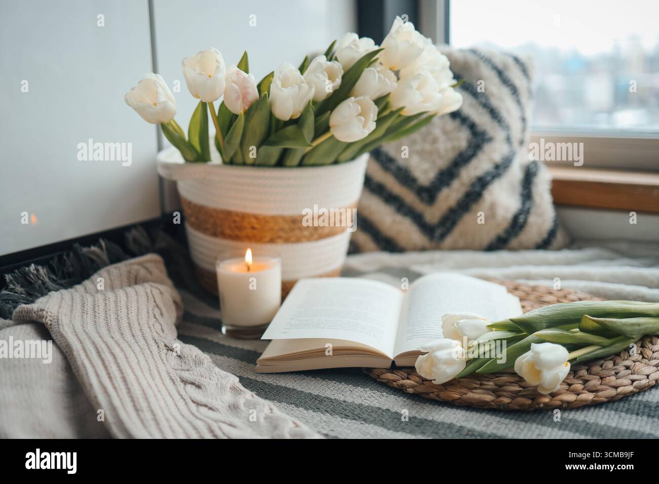 Livre ouvert, bougie et panier avec tulipes, composition confortable de printemps à l'intérieur de la maison. Banque D'Images