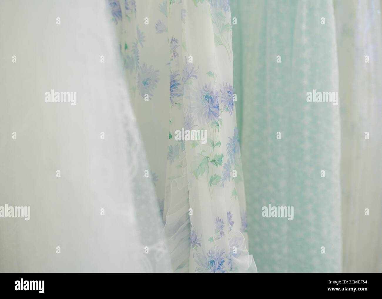 Robes florales transparentes dans des tons pastel accrochent gracieusement, ajoutant une touche d'élégance à l'espace lumineux. Banque D'Images