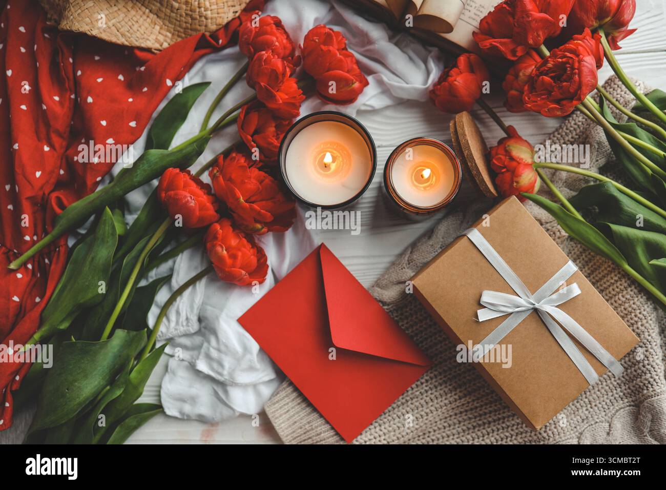 Composition festive vue de dessus pose à plat. Boîte cadeau, fleurs, enveloppe, bougies. Banque D'Images