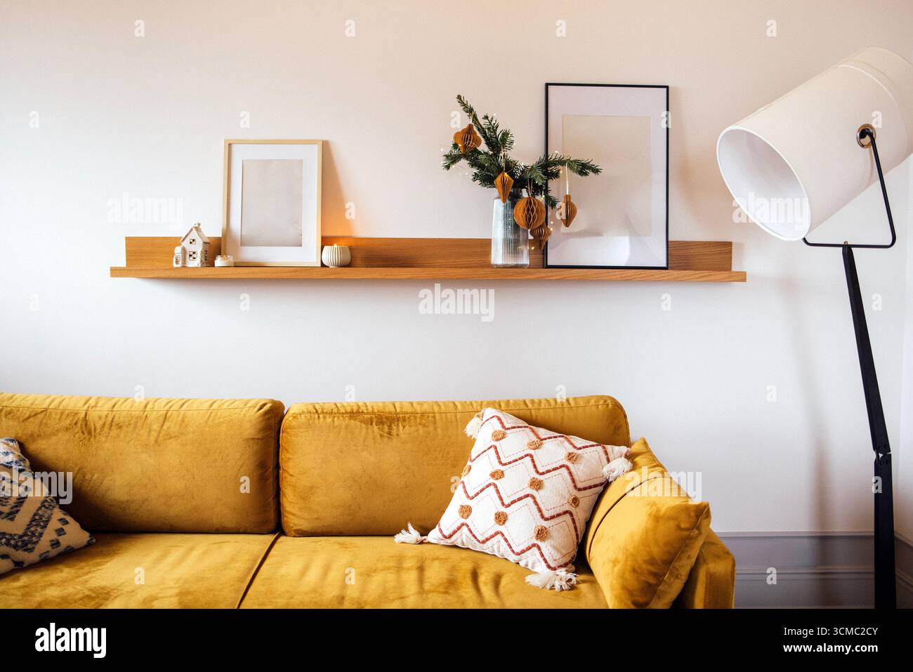 La scène accueillante du salon présente un canapé jaune moutarde avec des oreillers à motifs, une étagère en bois avec des objets décoratifs et un lampadaire moderne Banque D'Images