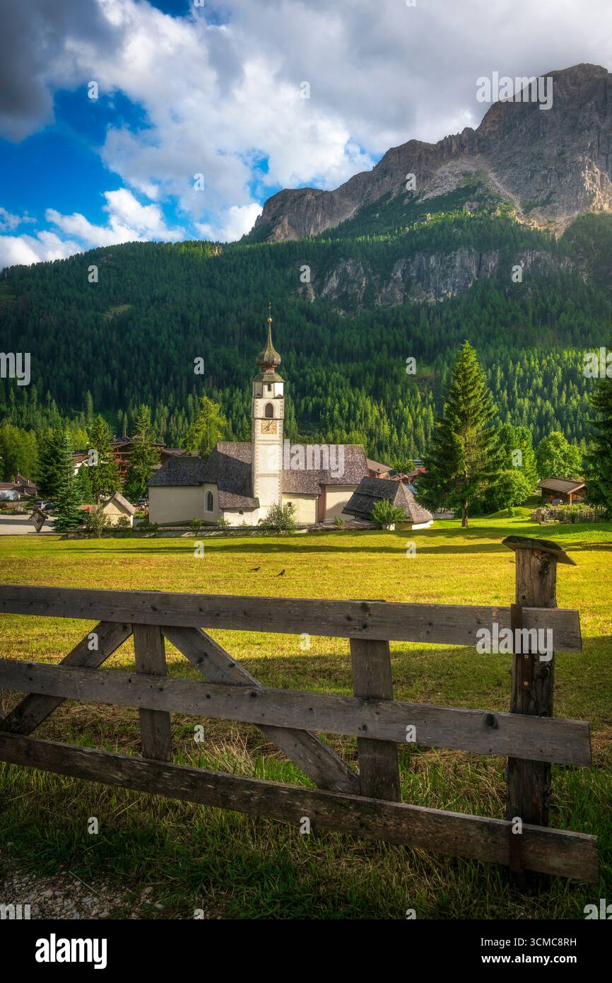 Pittoresque église alpine dans le village de Colfosco encadrée par une clôture en bois avec d'imposantes falaises calcaires des Dolomites et des prairies verdoyantes au coucher du soleil. Tyrol du Sud Banque D'Images Pittoresque église alpine dans le village de Colfosco encadrée par une clôture en bois avec d'imposantes falaises calcaires des Dolomites et des prairies verdoyantes au coucher du soleil. Tyrol du Sud Banque D'Images