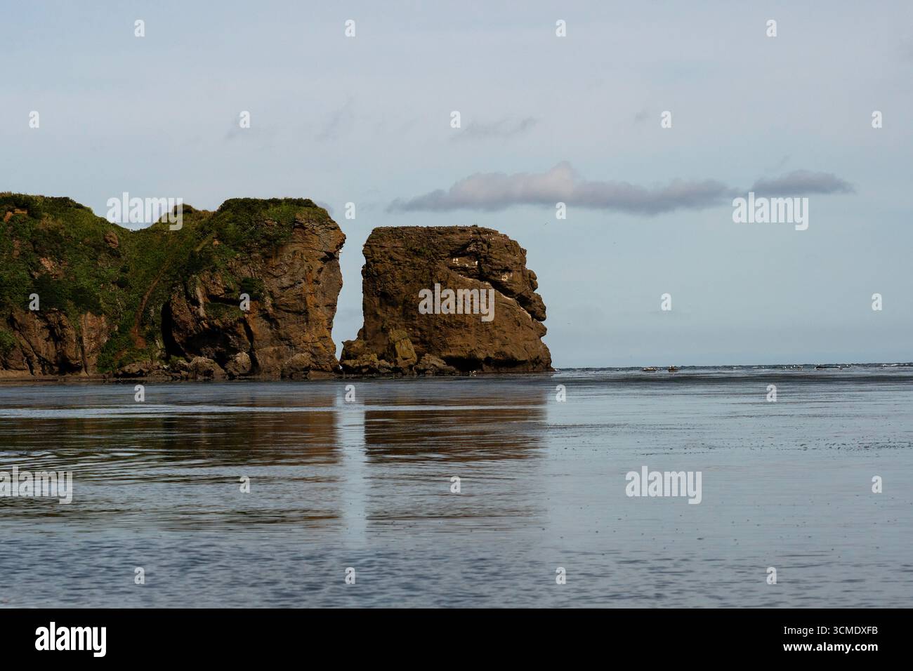 Une vue plus rapprochée d'une formation rocheuse côtière dramatique divisée par l'érosion, avec des falaises abruptes s'élevant au-dessus de la mer calme sous un ciel légèrement nuageux. TI Banque D'Images