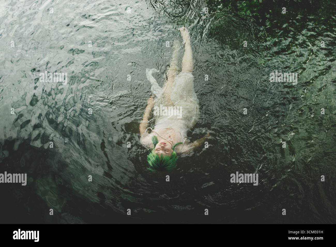 Femme élégante en robe de dentelle avec des cheveux verts se mélangeant à l'eau du lac, connexion surrea et harmonie de la nature Banque D'Images