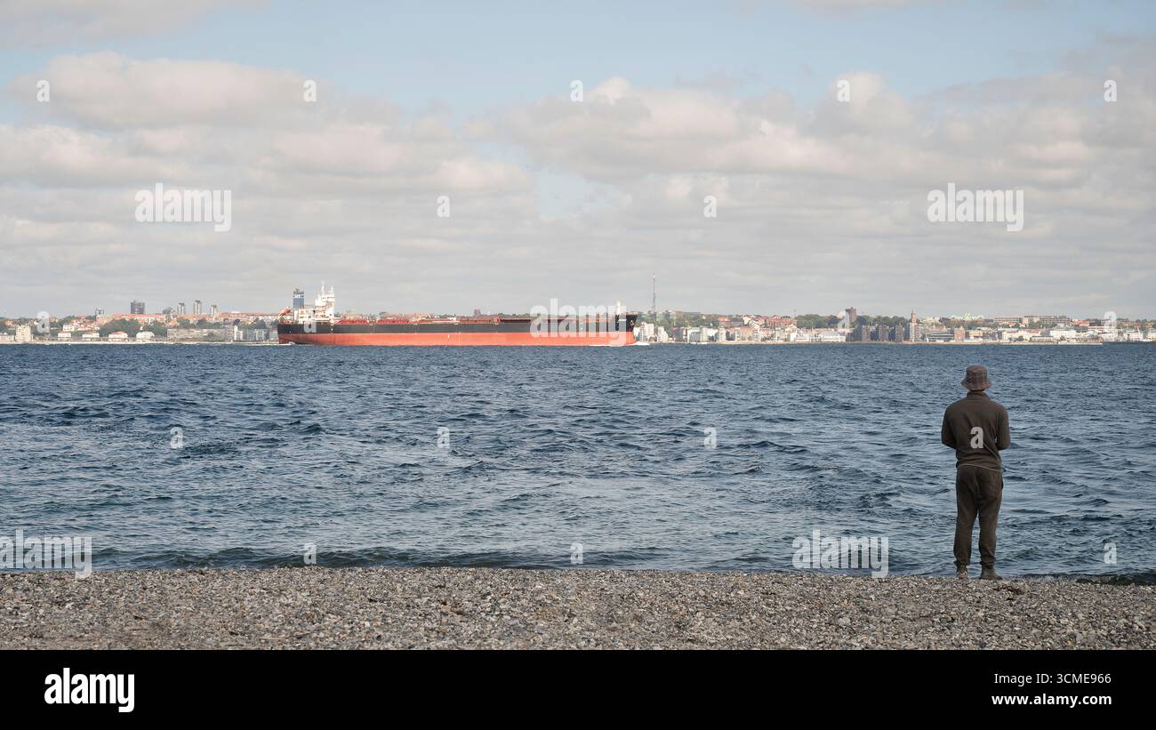 The Sound Öresund avec un pêcheur sur le rivage de galets en velokant un cargo dans le détroit, Elsinore, Danemark, août 2025 Banque D'Images
