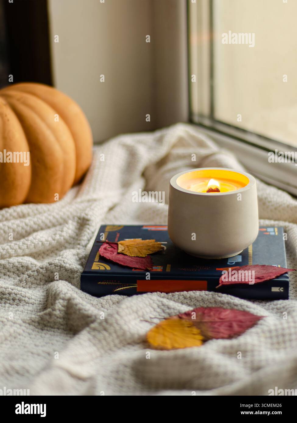 Vie morte d'automne confortable avec bougie, citrouille et feuilles colorées par fenêtre. Banque D'Images