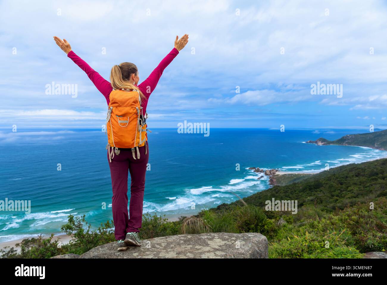 Femme athlétique sur le sentier de montagne, debout sur le rocher avec sac à dos et vue sur l'océan. Entraînement en plein air, trail running, randonnée pour la force, la santé et la forme Banque D'Images