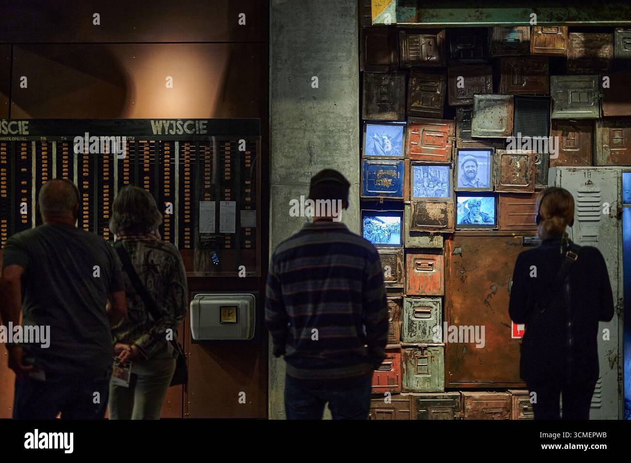 Un groupe de personnes observe des écrans numériques et des documents historiques sur un mur de musée, mettant en valeur la mémoire collective et l’engagement civique. Banque D'Images