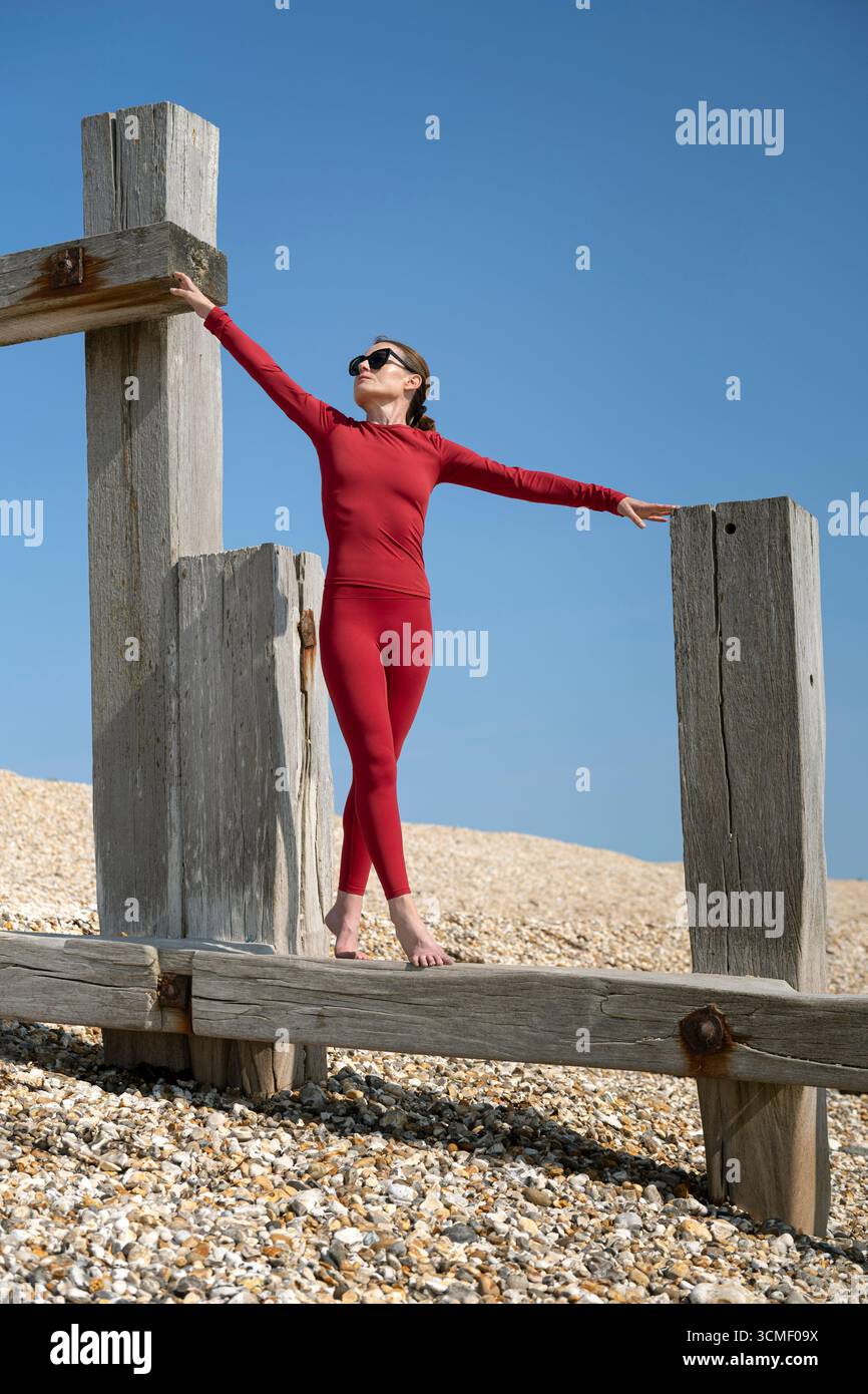 Femme en vêtements de sport rouges s'étirant gracieusement sur la structure en bois à l'extérieur à la plage Banque D'Images