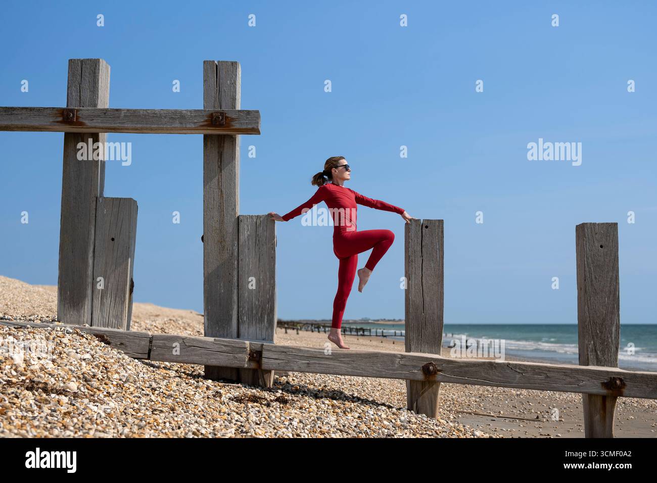 Femme en vêtements de sport rouges s'étirant gracieusement sur la structure en bois à l'extérieur à la plage Banque D'Images