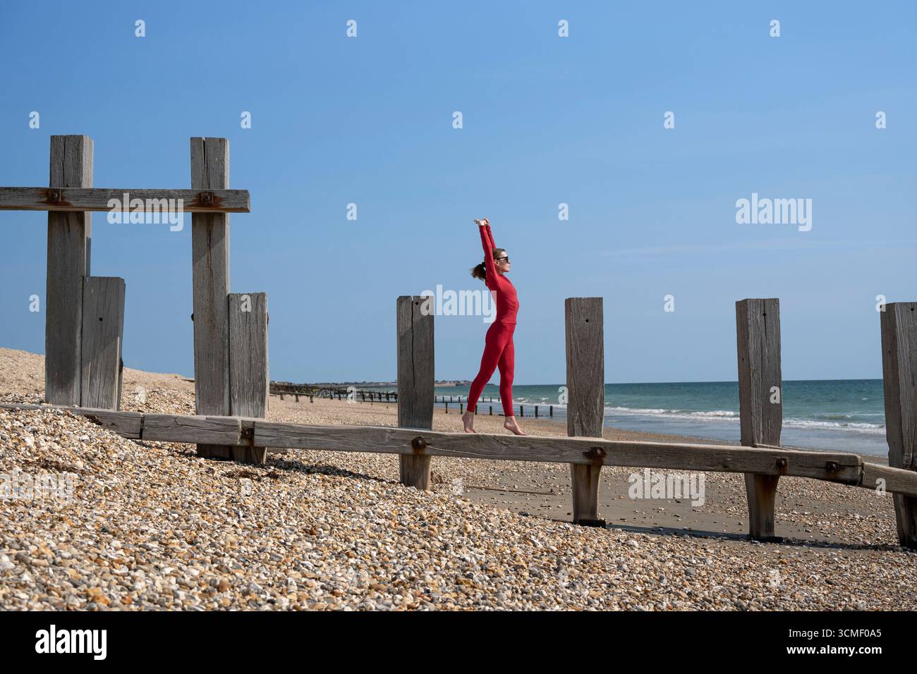 Femme en vêtements de sport rouges s'étirant gracieusement sur la structure en bois à l'extérieur à la plage Banque D'Images