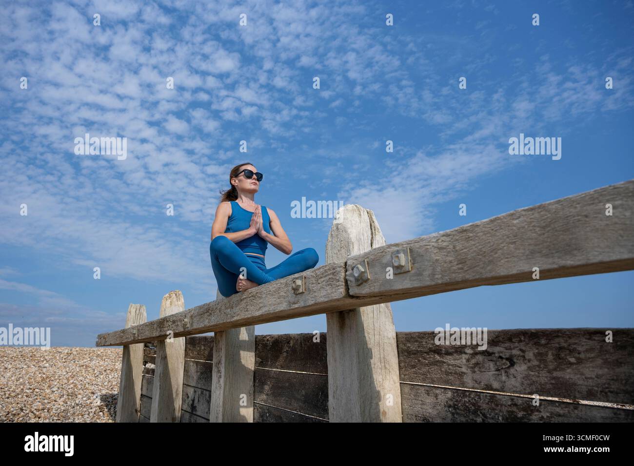 Femme sportive pratiquant le yoga et méditant en plein air sur une structure en bois sous un ciel bleu Banque D'Images