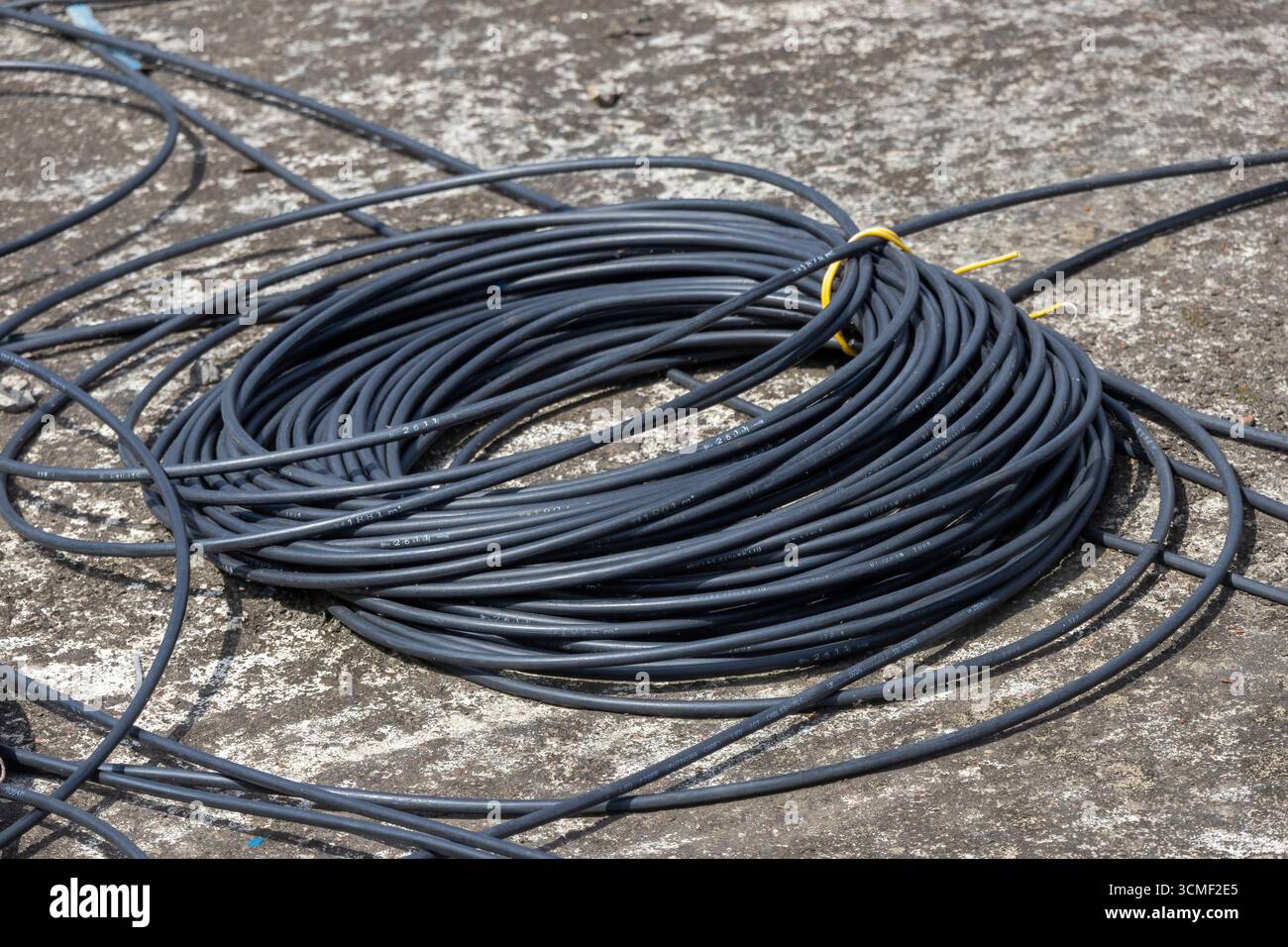 Gros plan d'une bobine de fils électriques noirs, ou de câbles, sur un sol en béton gris, mettant en évidence les thèmes industriels, de la construction et de l'alimentation. Banque D'Images