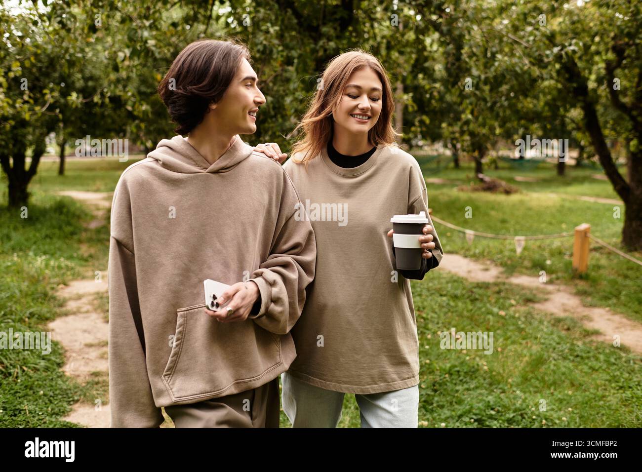 Un couple aimant marche main dans la main, riant dans un cadre extérieur paisible entouré d'arbres. Banque D'Images