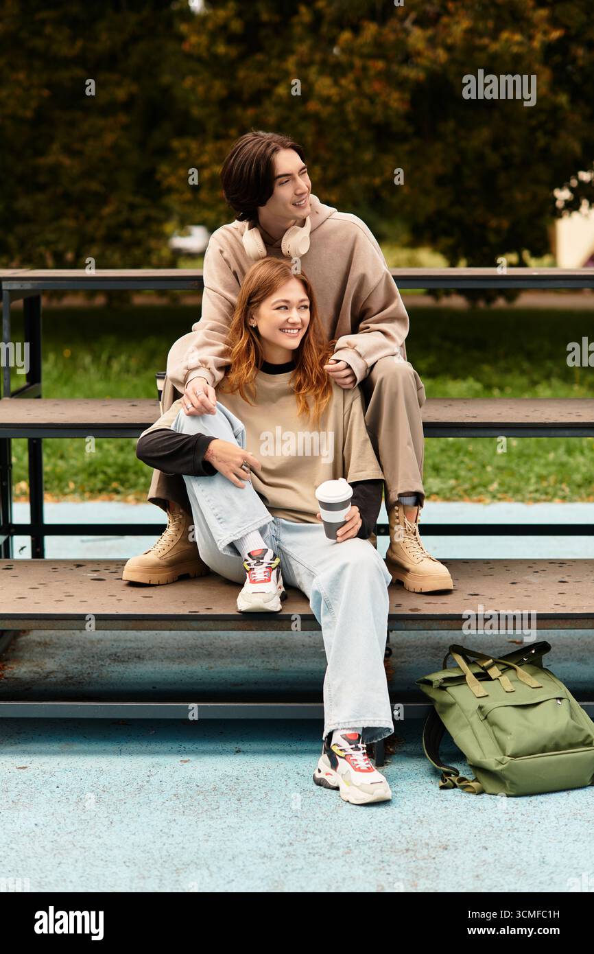 Un jeune couple partage une étreinte chaleureuse tout en étant assis sur un banc, entouré par la nature et la joie. Banque D'Images