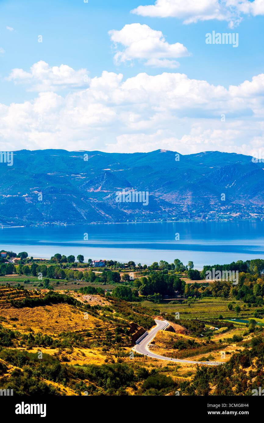 Vue panoramique sur le lac Ohrid depuis l'Albanie avec route sinueuse, champs verts et montagnes sous un ciel bleu vif avec des nuages moelleux Banque D'Images