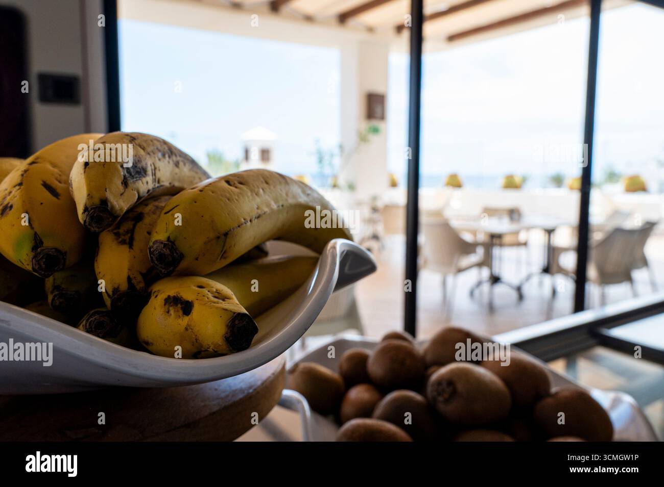 Un bol de bananes se trouve sur une table devant une fenêtre. Les bananes sont mûres et prêtes à manger. La scène est accueillante et confortable, avec les bananes et ot Banque D'Images