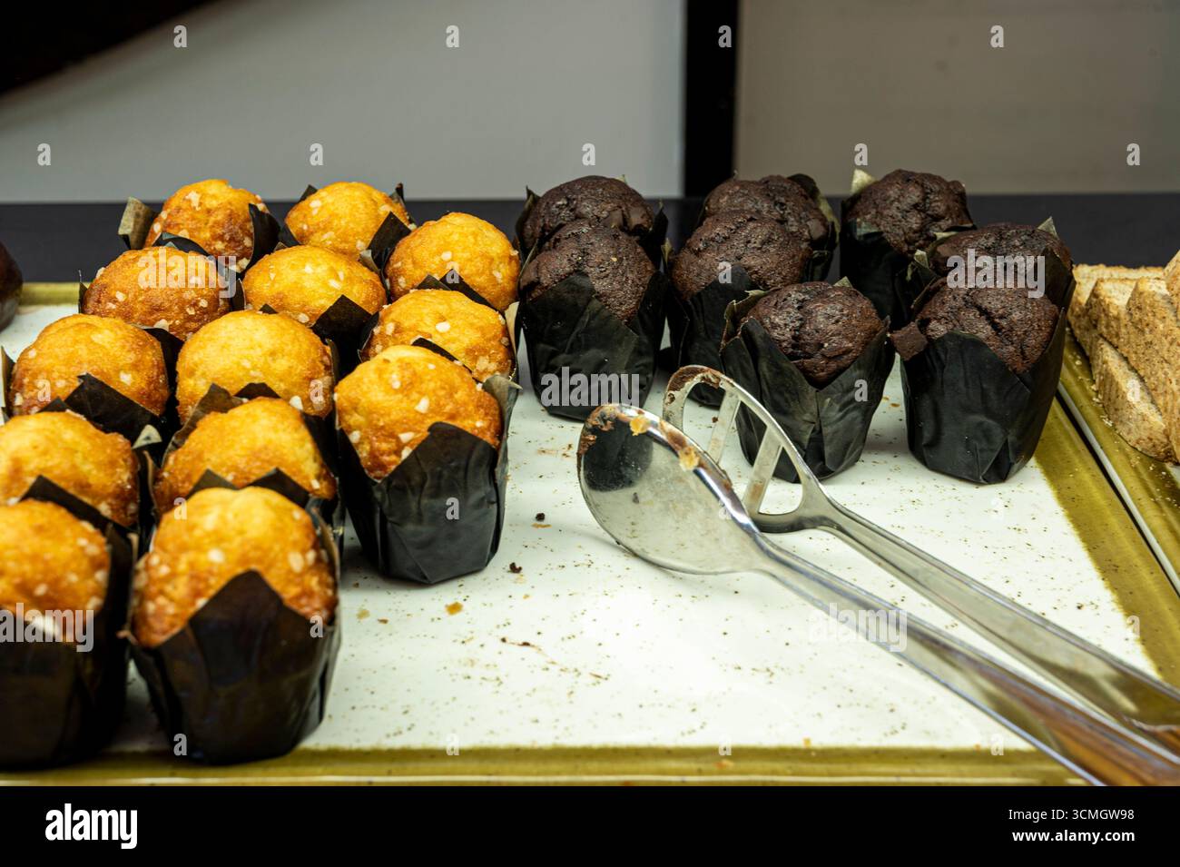 Un plateau de muffins et une cuillère sont sur une table. Les muffins sont de différentes couleurs et saveurs, y compris le chocolat et la vanille. Banque D'Images