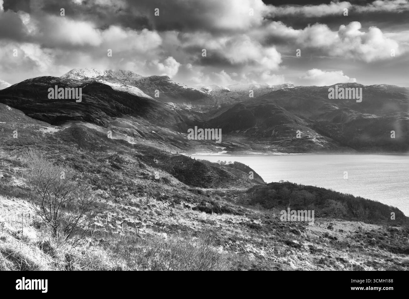 Un paysage monochrome montre des montagnes enneigées qui rencontrent un loch, soulignant la beauté sauvage des Highlands écossais. Banque D'Images