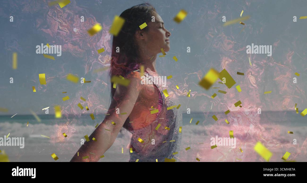 Femme debout portant un haut orange en salopette, fermant les yeux sur la plage, confettis dorés, tourbillon rose Banque D'Images