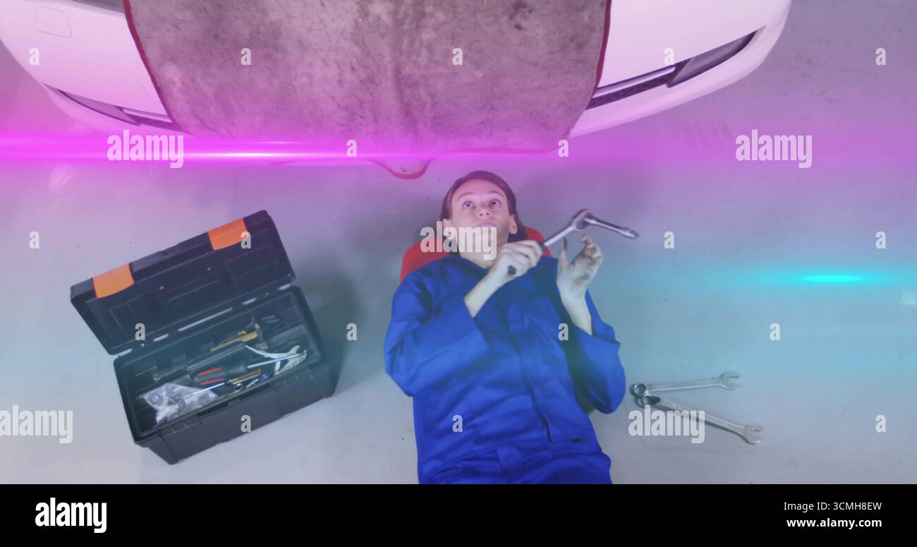 Femme mécanicien dans des combinaisons couchées sous la voiture à l'aide d'une clé et d'une barre d'extension dans le garage Banque D'Images