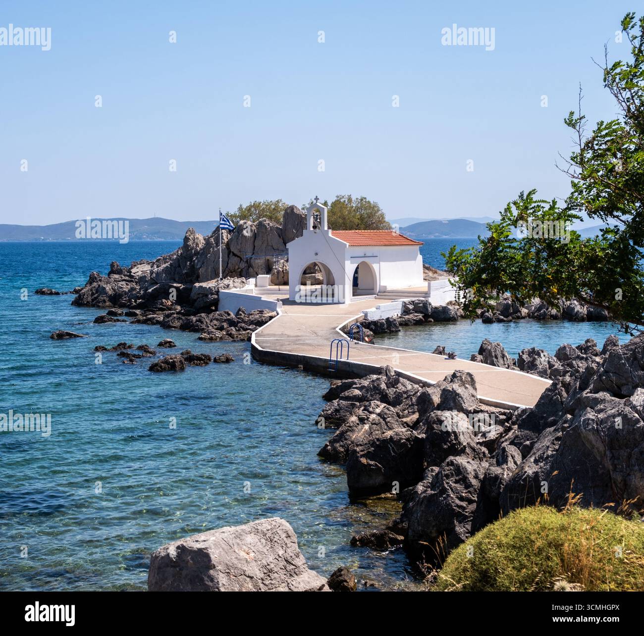 Chios, petite église d'Agios Isidoros, Grèce. Chapelle d'architecture traditionnelle avec toit de tuiles rouges et clocher sur les rochers, journée d'été ensoleillée Banque D'Images