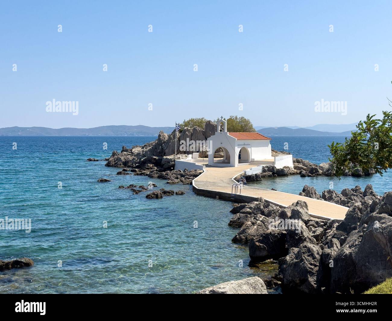 Chios, petite église d'Agios Isidoros, Grèce. Chapelle d'architecture traditionnelle avec toit de tuiles rouges et clocher sur les rochers, journée d'été ensoleillée Banque D'Images