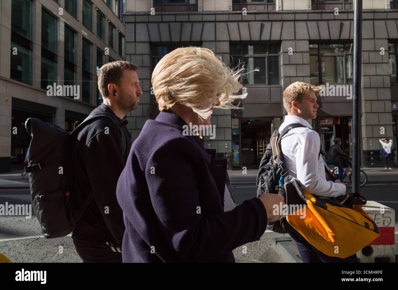 Les navetteurs de la ville de Londres ayant une mauvaise journée de cheveux alors que de fortes rafales de vent soufflent sur Bishopsgate pendant l'heure du déjeuner au cœur de la ville de Londres, au Royaume-Uni Banque D'Images
