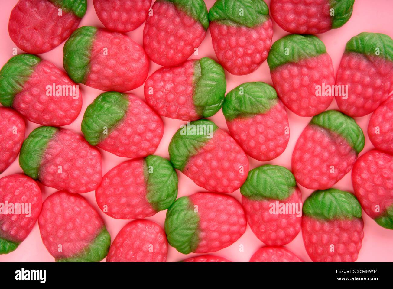 De nombreux bonbons en forme de fraise formant un motif coloré et appétissant sur un fond rose Banque D'Images