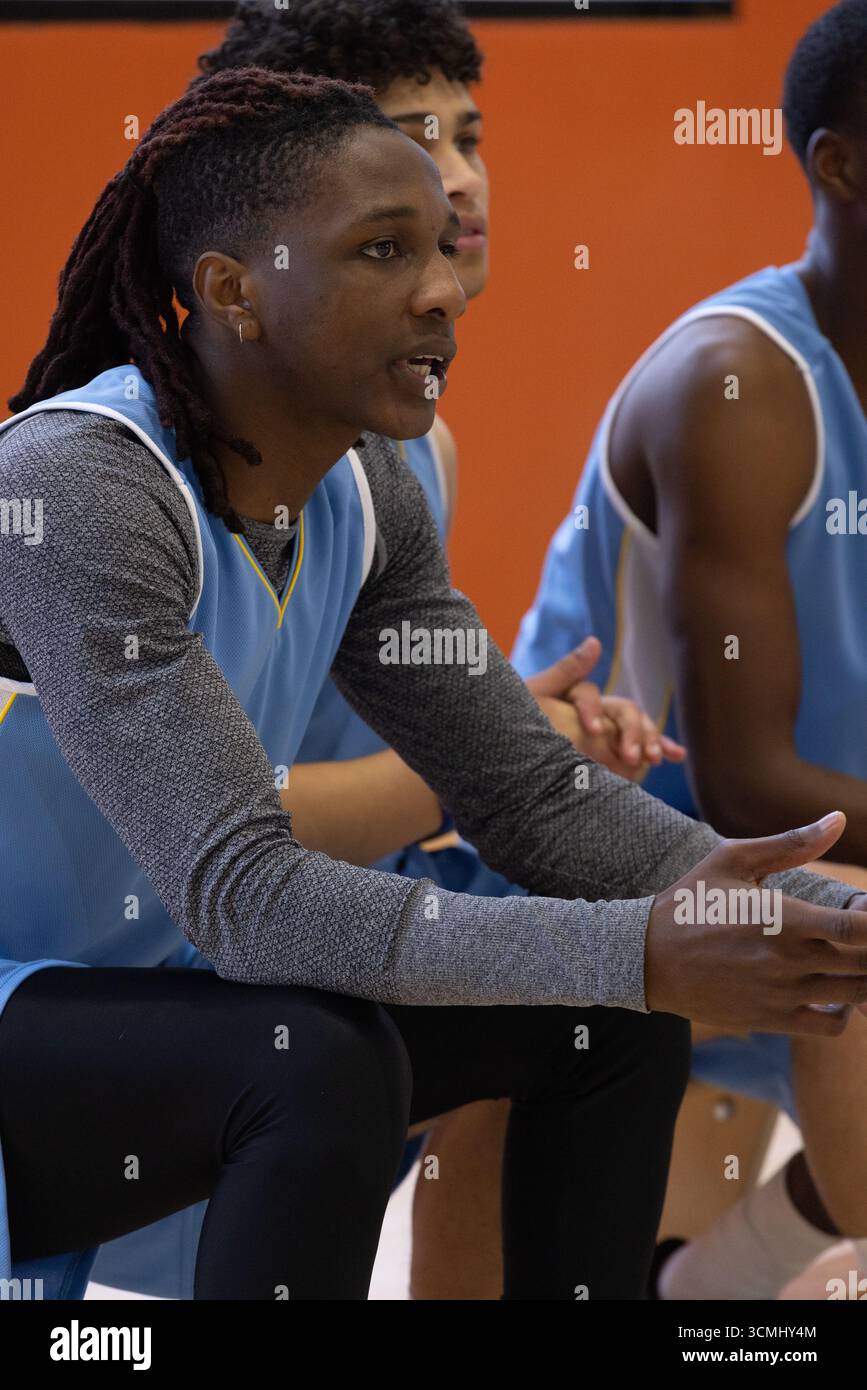 Divers coéquipiers masculins assis sur un banc en bois sur le banc de touche de la salle de sport portant des uniformes bleu clair Banque D'Images