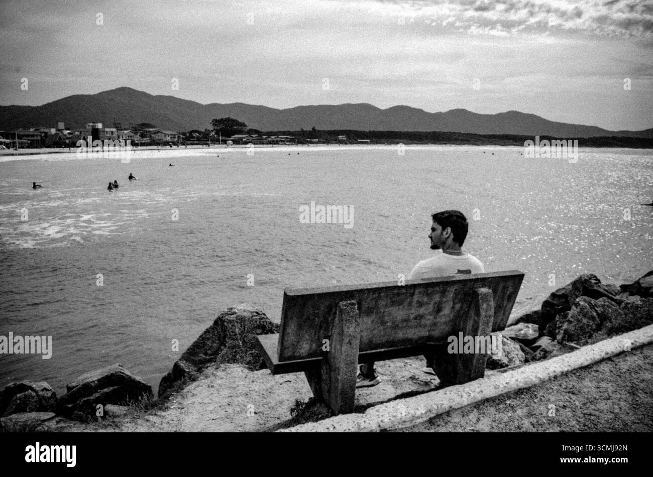Homme assis sur le banc face à l'océan à Barra da Lagoa, Florianópolis, Santa Catarina, Brésil noir et blanc photo d'art Banque D'Images