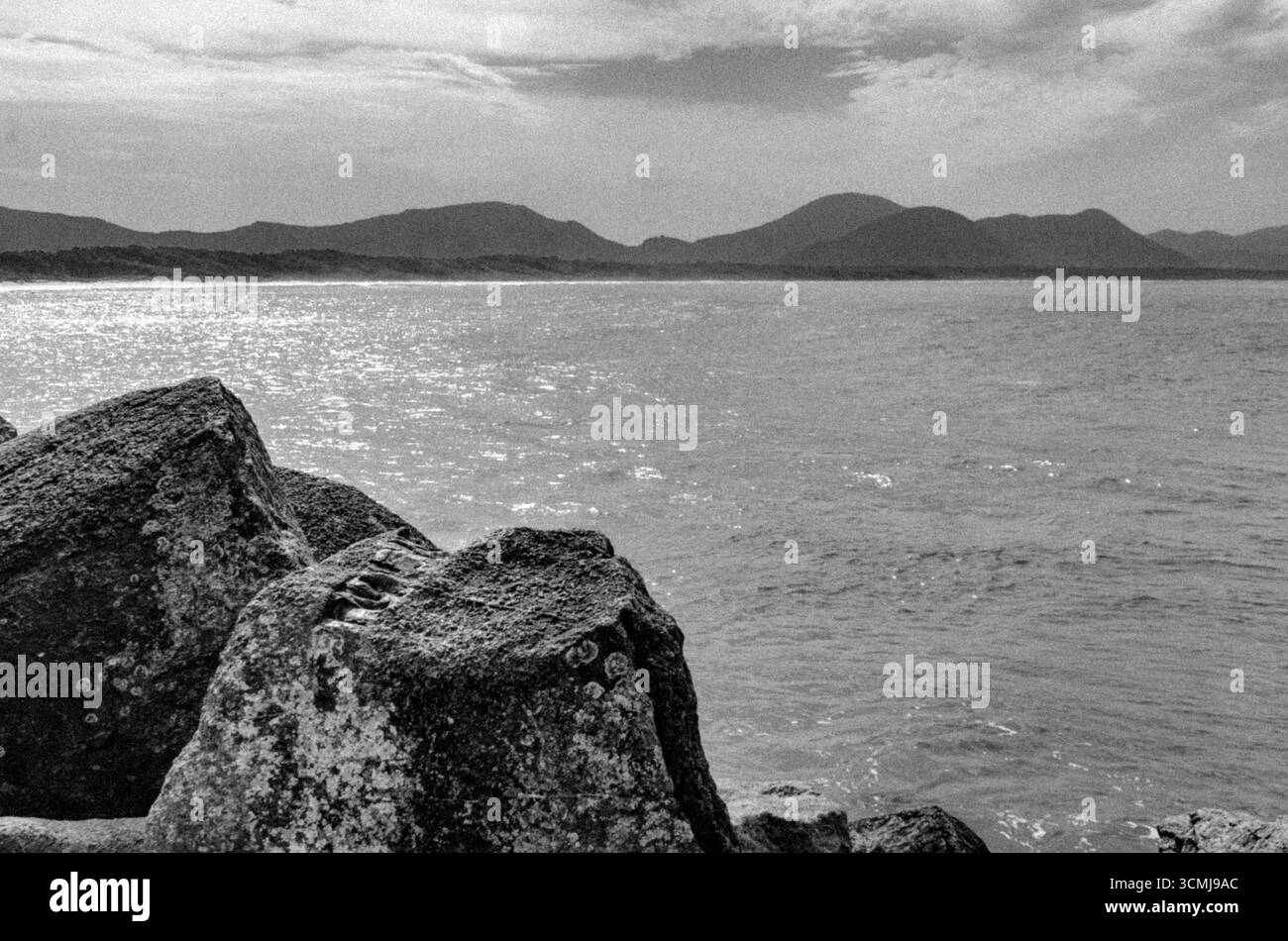 Rivage rocheux et montagnes lointaines à Barra da Lagoa, Florianópolis, Santa Catarina, Brésil - paysage marin noir et blanc d'océan calme et de beauté naturelle Banque D'Images