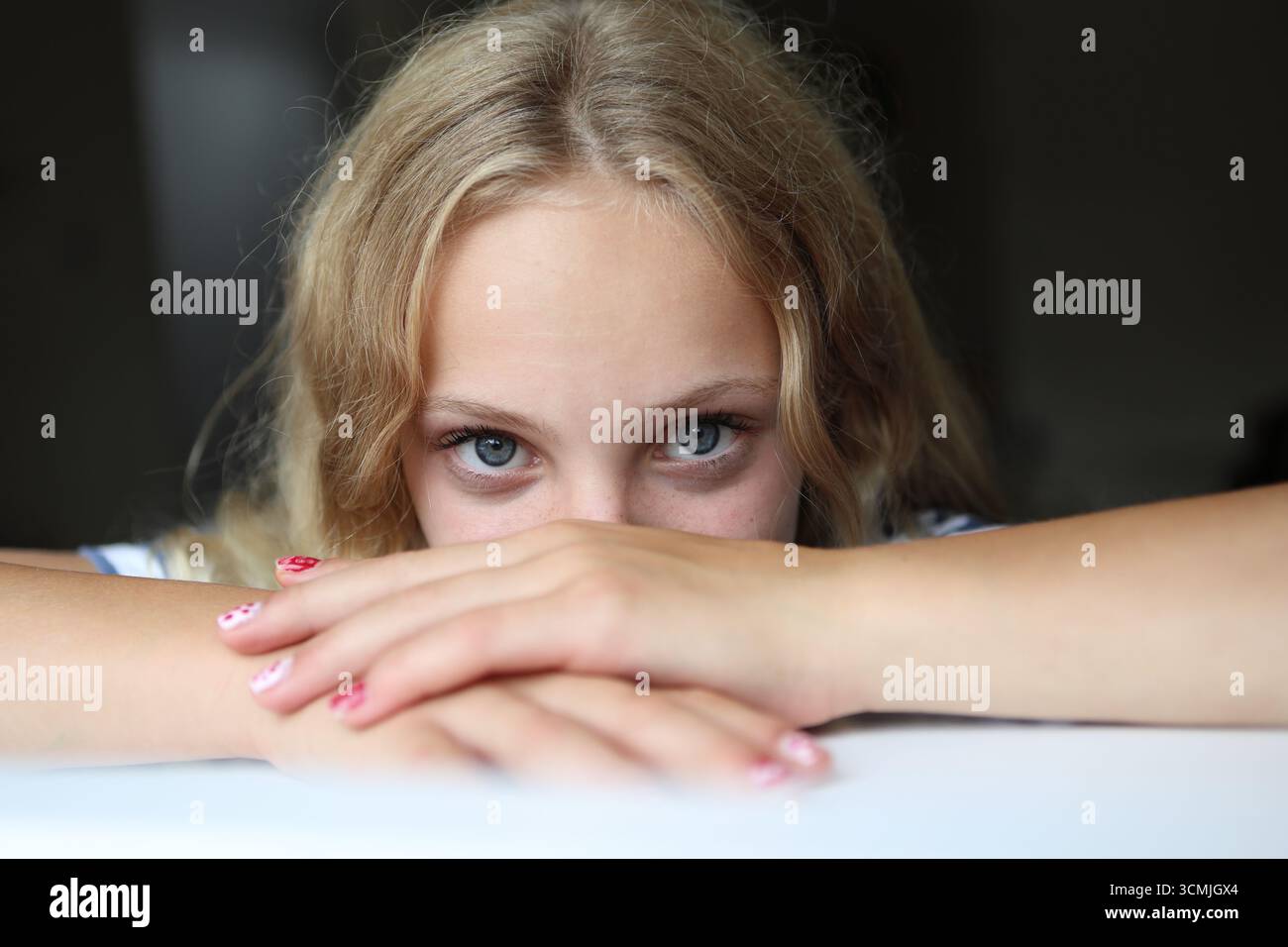 Fille appuyée sur le rebord de la fenêtre regardant par la fenêtre avec les mains près du visage regard intense contact direct avec les yeux Banque D'Images