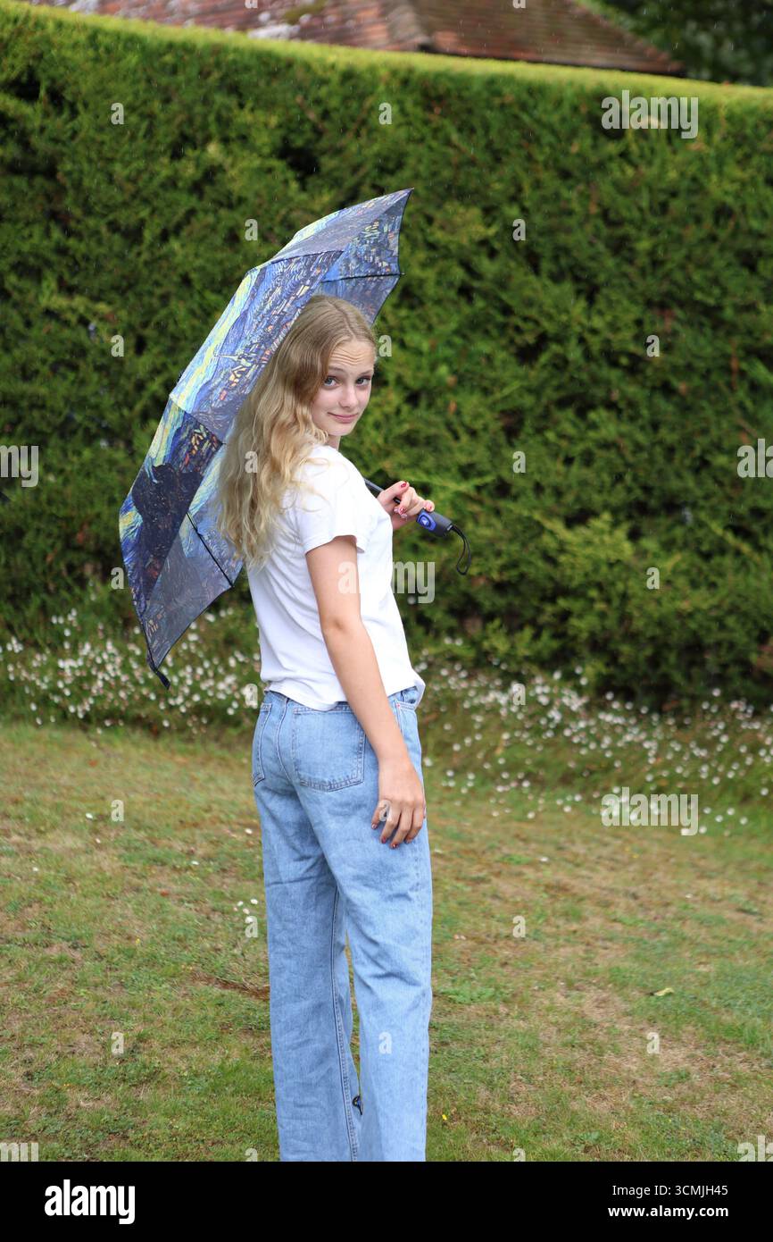 Fille avec un parapluie dans le jardin regardant directement le contact visuel regardant par-dessus l'épaule Banque D'Images