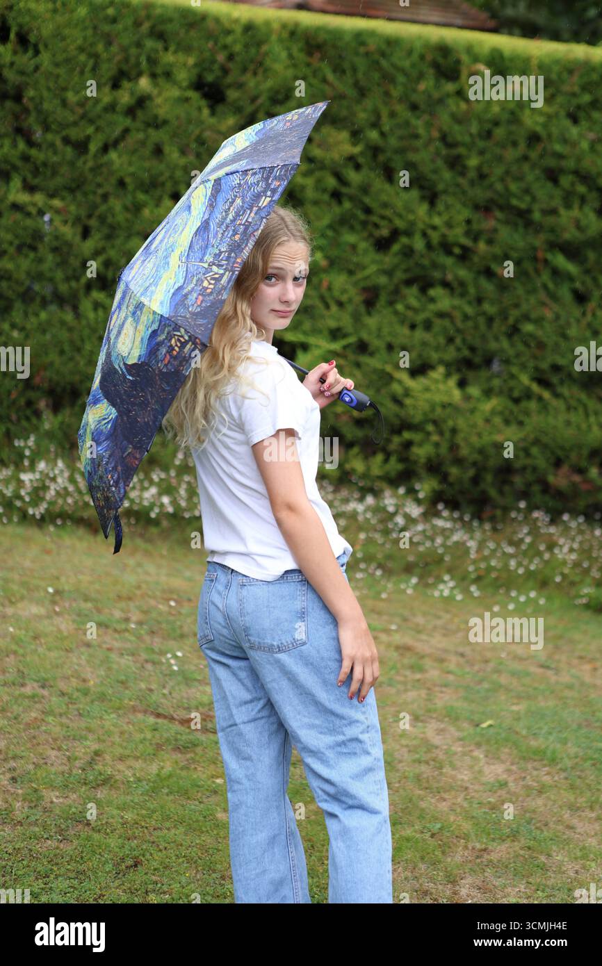 Fille avec un parapluie coloré dans le jardin regardant directement les yeux regardant par-dessus l'épaule Banque D'Images