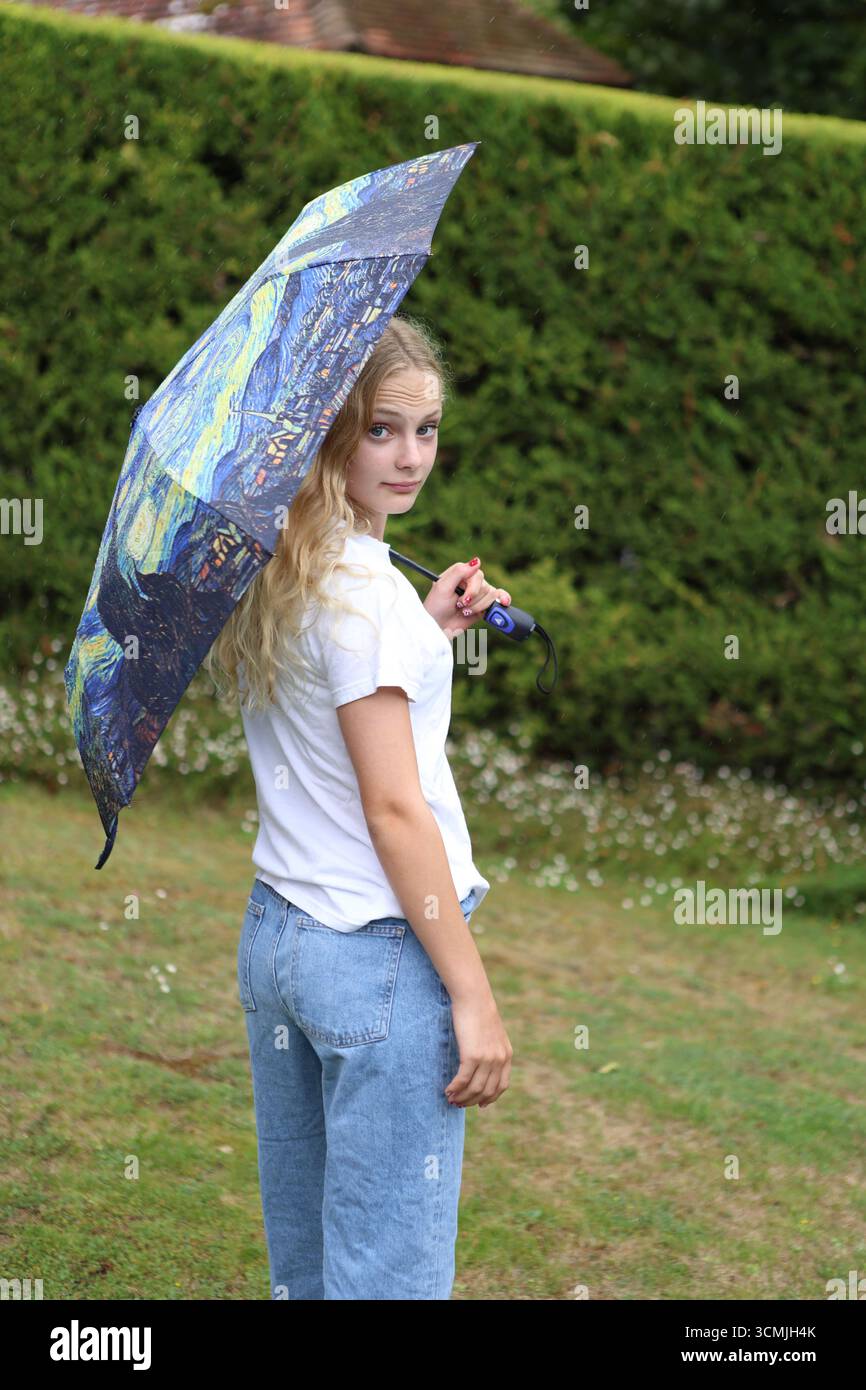 Fille avec un parapluie coloré dans le jardin regardant directement les yeux regardant par-dessus l'épaule Banque D'Images