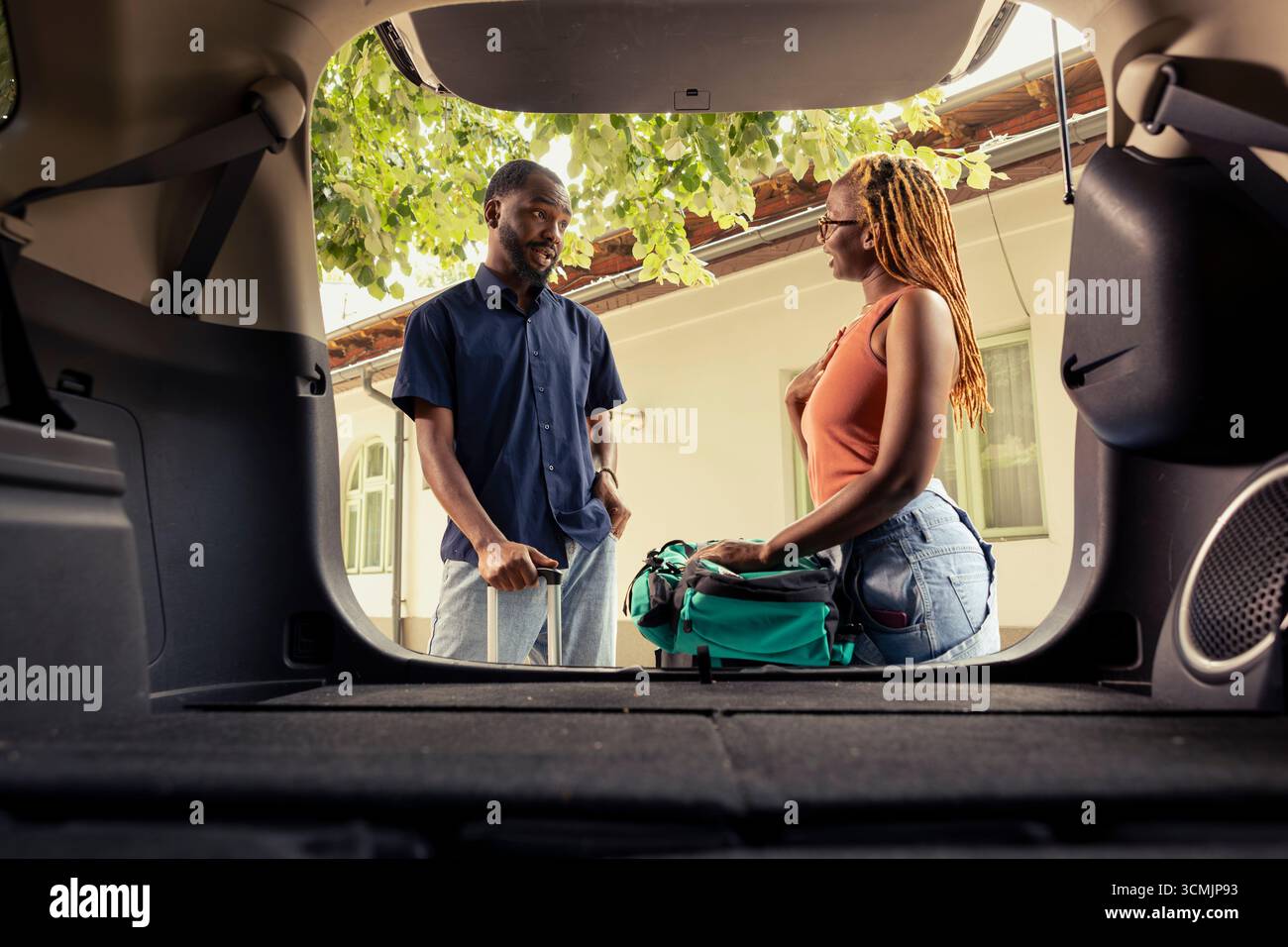 Homme noir et femme chargeant des bagages dans la voiture se préparant pour le voyage automatique, entouré de valises et soleil d'été dans l'allée. Aventure joyeuse avec plaisir et voyage de loisirs ensemble. Banque D'Images