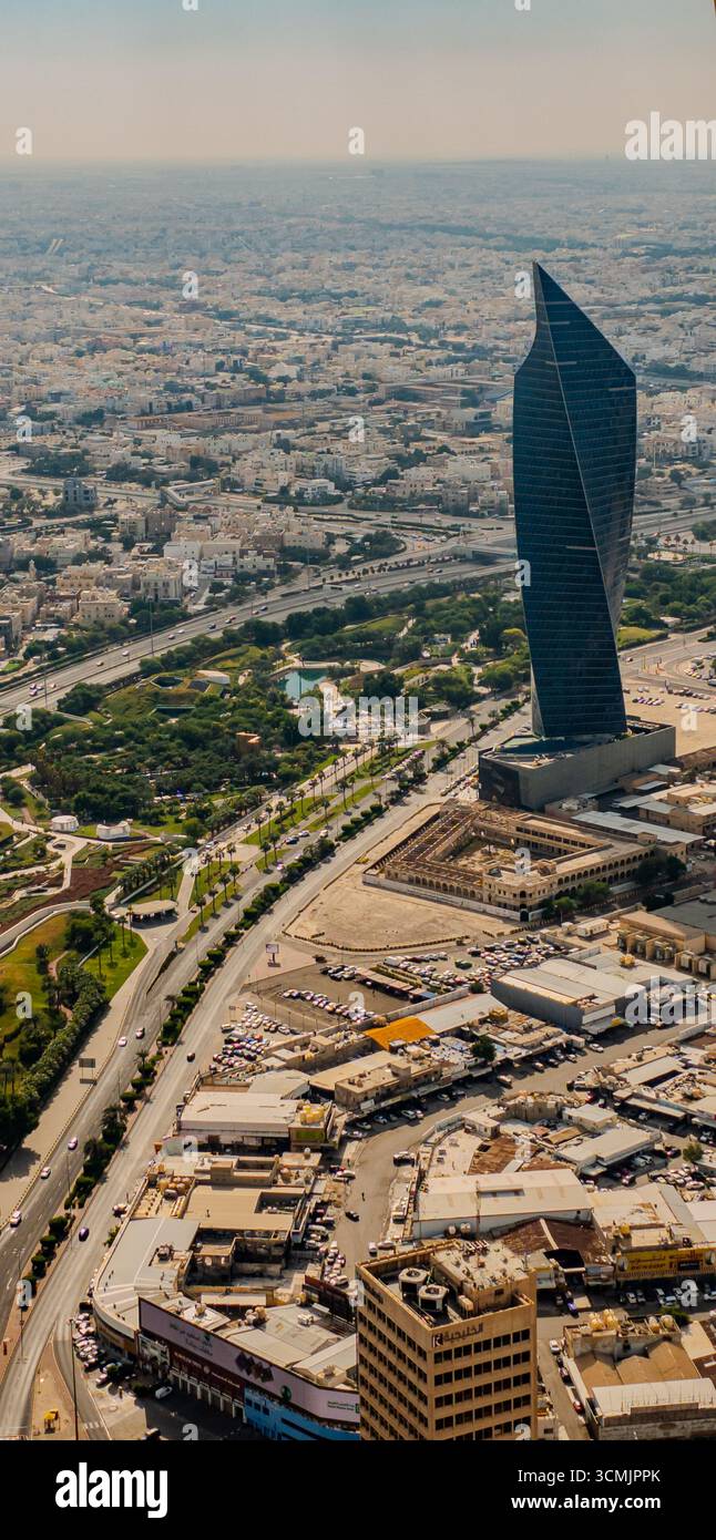Vue aérienne de Koweït City mettant en valeur la tour Tijaria, un gratte-ciel au design unique, entouré de structures urbaines, de routes et d'espaces verts. Banque D'Images