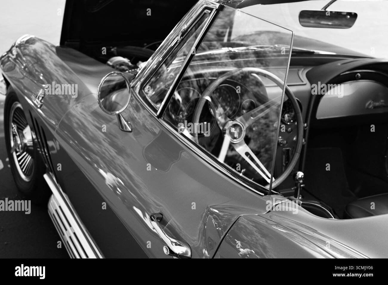 Photo en noir et blanc d'une voiture ancienne avec volant en bois et tableau de bord détaillé. Design intérieur et extérieur automobile classique capturé dans TI Banque D'Images