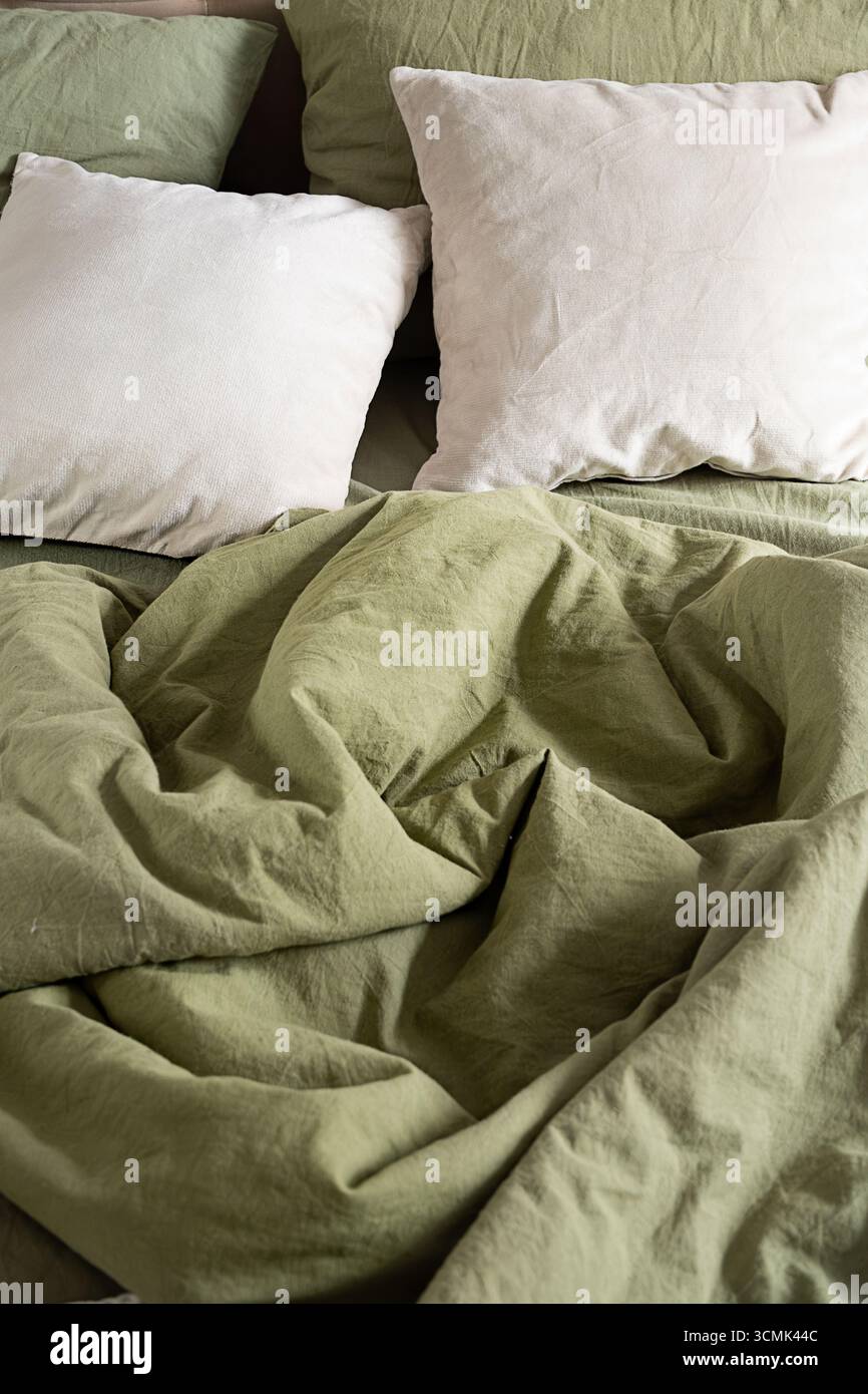 Literie verte froissée avec oreiller blanc sur le lit. Concept de couchage confortable, intérieur de maison confortable et de détente. Banque D'Images