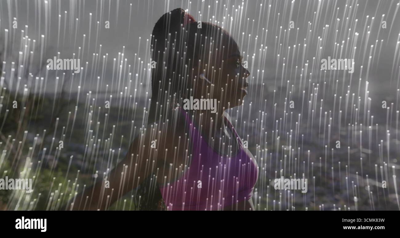 Coureur noir debout portant un soutien-gorge de sport violet et des écouteurs blancs à flanc de colline, avec des stries de pluie Banque D'Images